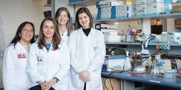 Dr. Carolina Tropini (seated) and her team of 3 other women in a lab surrounded by equipment