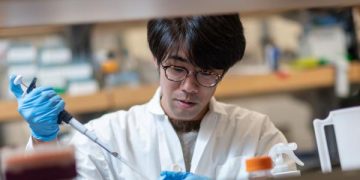 Young student, asian male, in white lab jacket and medical gloves holding a pipette in a lab