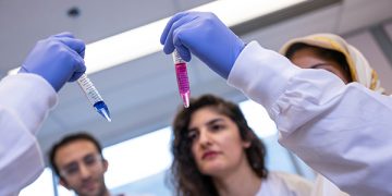 small group of lab workers hold up two test tubes filled with brightly coloured liquids