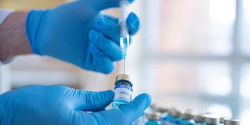 Photo of a medical researcher in gloves holding a vial with a syringe