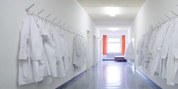 A series of white lab coats on hooks in a biomedical facility